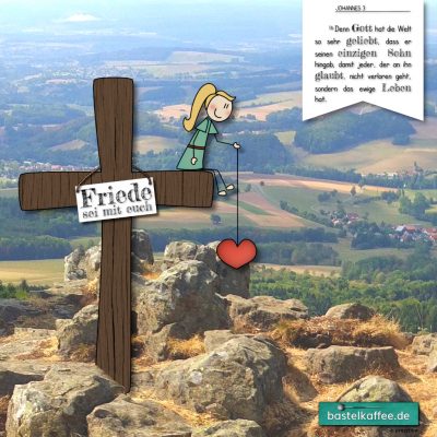 Blick von einem Berg ins Tal auf Wälder, Wiesen und Dörfer. Auf dem Berg steht ein Kreuz auf dem ein Mädchen sitzt und ein Herz in der Hand hält. Am Kreuz hängt ein Schild, auf dem "Friede sei mit euch" steht.